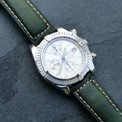 Berlin green full grain leather watch strap on the Breitling Evolution Chronomat. Placed diagonally on a slate background.
